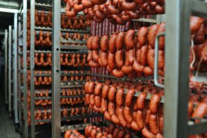 a lot of smoked sausages on the metal shelves of the racks of the meat factory.